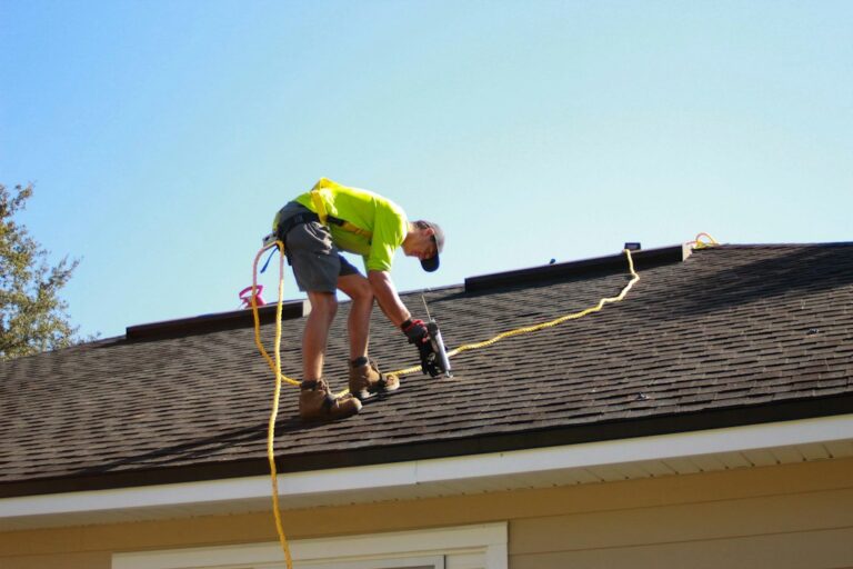 Roofing workers inspect exposed roof decking beside newly installed underlayment and flashing.